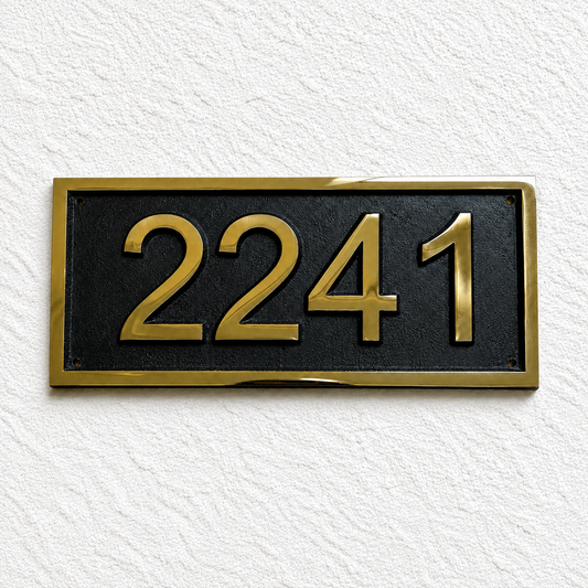 A rectangular house number plaque with the gold numerals '2241' on a black background, bordered by a gold frame, mounted on a textured white wall.
