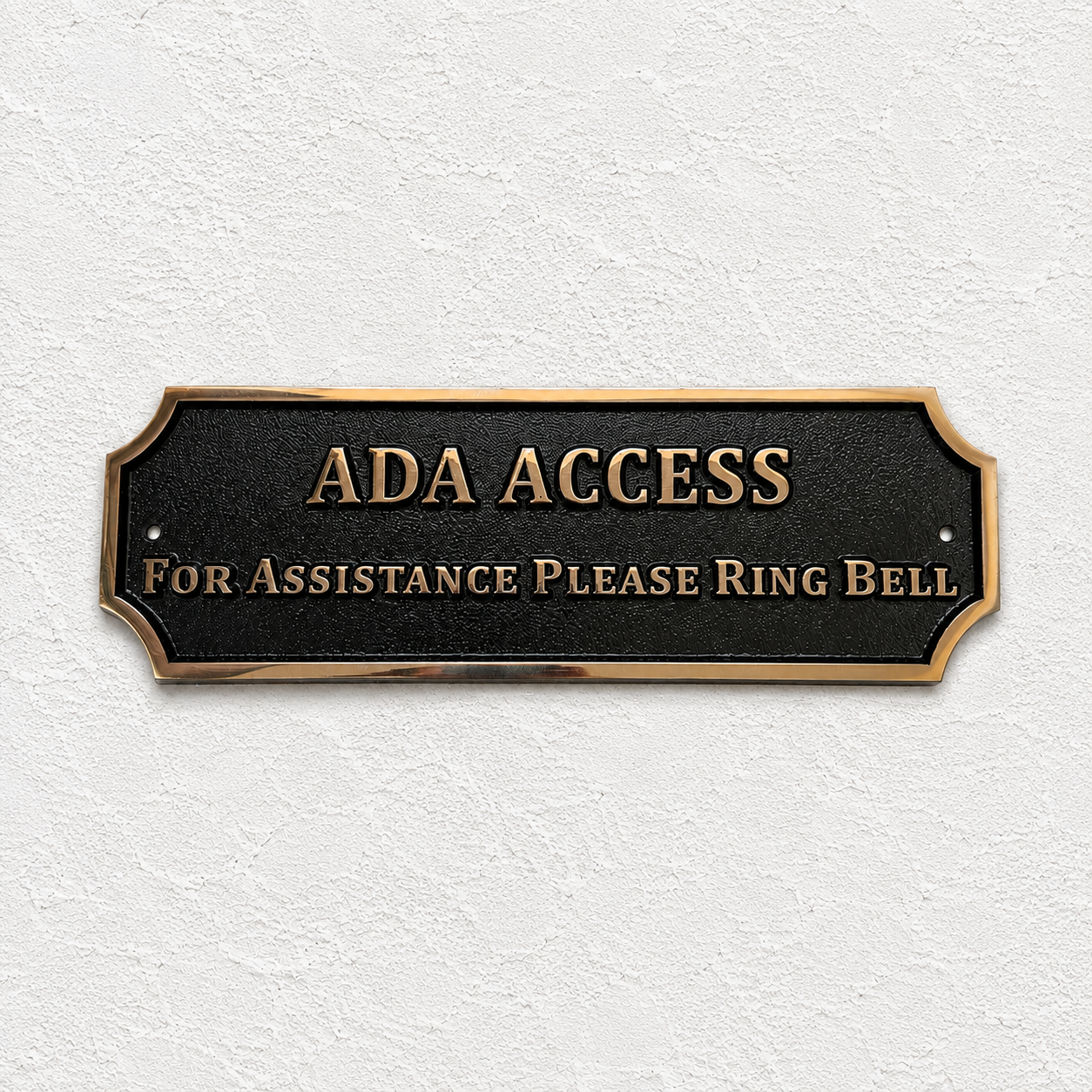 ADA Access sign with raised gold lettering on a black plaque, mounted on a textured white wall.