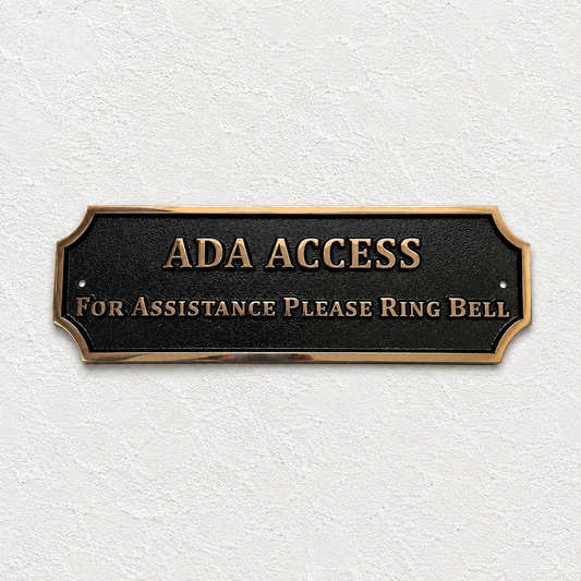 ADA Access sign with raised gold lettering on a black plaque, mounted on a textured white wall.