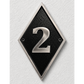 A diamond-shaped black house number plaque with a silver metallic border and the number '2' in raised silver lettering, mounted on a textured white wall.