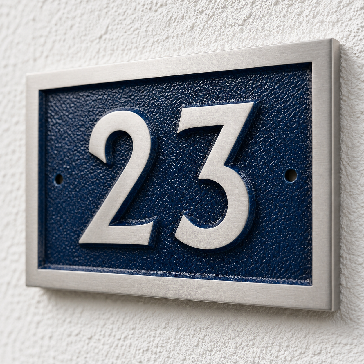 A modern house number plaque featuring the numbers '23' in raised silver lettering on a dark textured blue background, mounted on a white textured stucco wall.