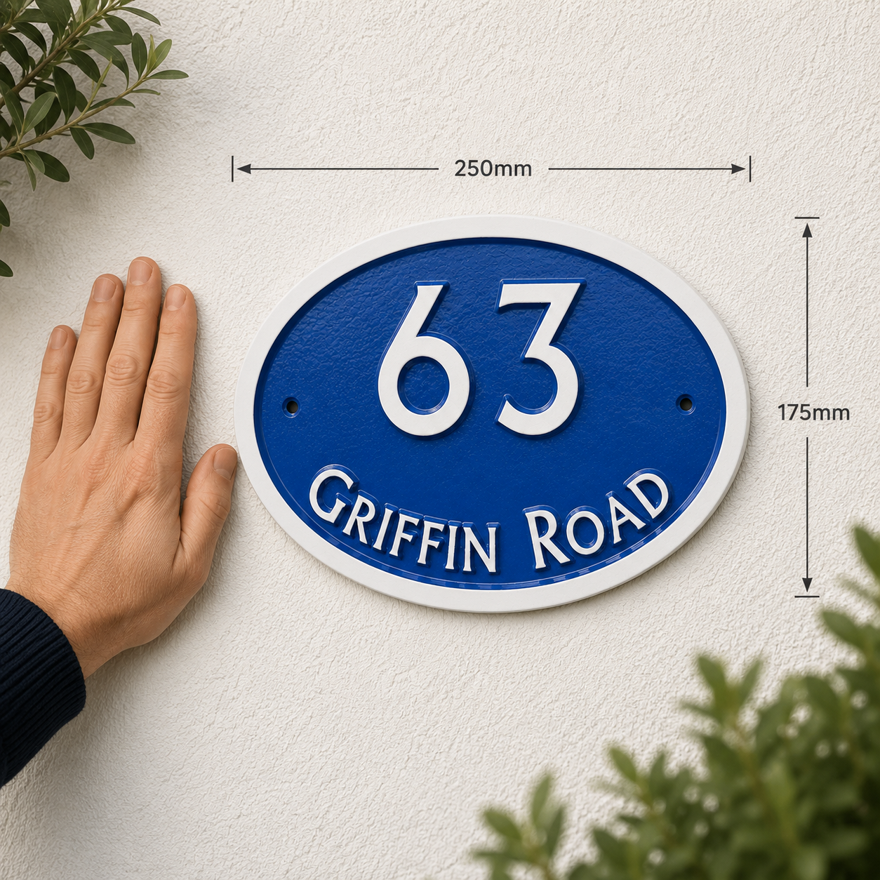 Blue and white oval house number 63 on Griffin Road wall plaque with dimension arrows showing 250mm by 175mm, next to a person's hand for scale.
