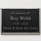 A rectangular black memorial plaque with a brushed silver border, mounted on a white textured wall. The plaque features raised silver lettering that reads 'In memory of Roy Webb 1936 - 2025 Derek & Helen Bell-Jones'.