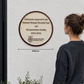 A round bronze and white National Heritage Memorial Fund commemorative plaque mounted on a white textured wall, with a woman standing to the right viewing it. A dimension line below the plaque indicates 400mm width.