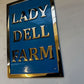 Blue sign with gold text 'LADY DELL FARM' on a white wall