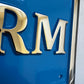 Close-up of a blue sign with gold letters 'RM' on a white background