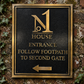 A rectangular black metal sign with a gold border and gold lettering mounted on a weathered brick wall with ivy. The sign reads 'No 1 House Entrance Follow Footpath to Second Gate' with a left-pointing arrow at the bottom.