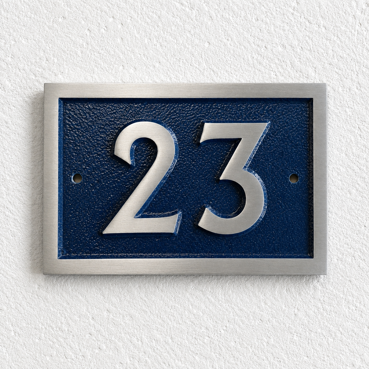 A rectangular house number plaque with raised silver numerals '23' on a textured dark blue background, mounted on a white textured wall.