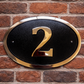 Cast bronze oval house number sign with polished raised numeral and black background
