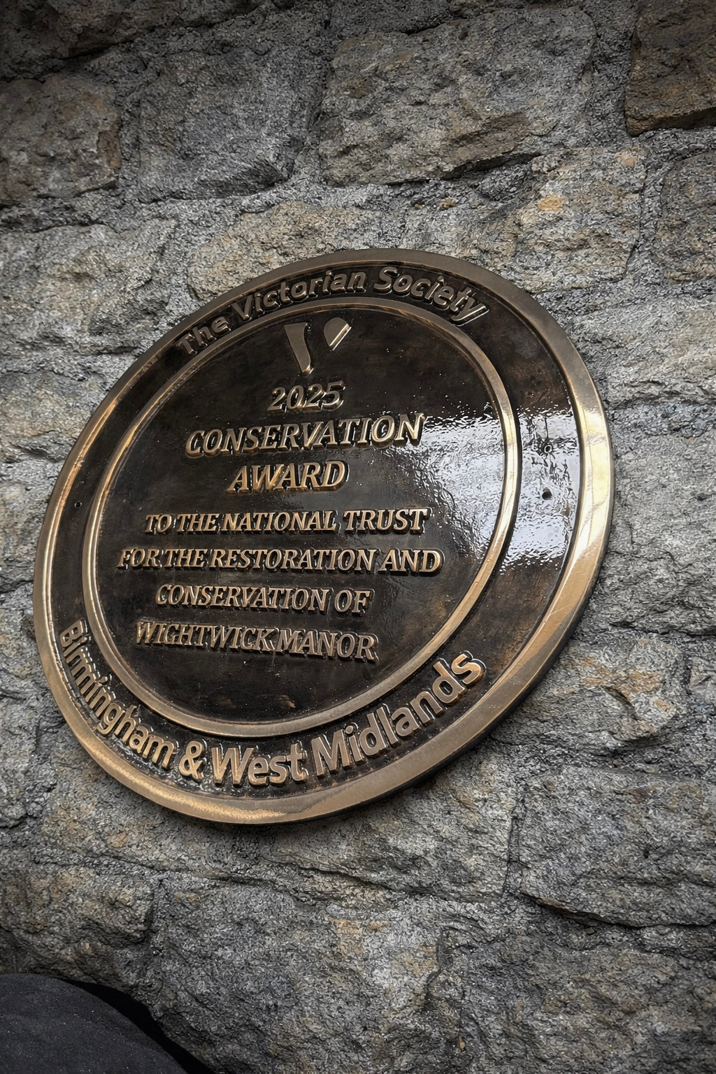 Cast bronze circular heritage plaque with raised lettering mounted on exterior wall