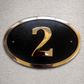 Cast bronze oval house number sign with polished raised numeral and black background

