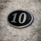 Cast aluminium oval hotel room number sign with raised numbers and black background mounted on wall