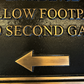 Close-up of a black metal sign with raised gold lettering reading 'ENTRANCE' and 'SECOND GA.