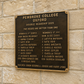 A bronze commemorative plaque for Pembroke College Oxford Double Headship 2025 mounted on a beige stone wall. The plaque features raised gold lettering listing the women's and men's top 8 players and coaches.