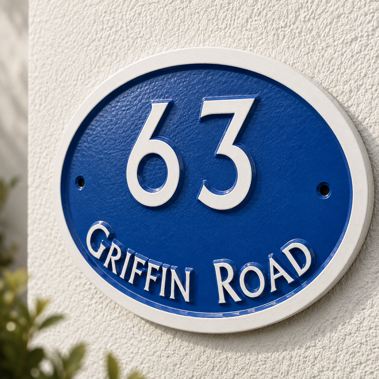 An oval blue and white house number plaque reading '63 GRIFFIN ROAD' mounted on a textured white stucco wall.