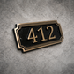 Cast bronze rectangle house number sign with raised numbers and double border mounted on exterior wall