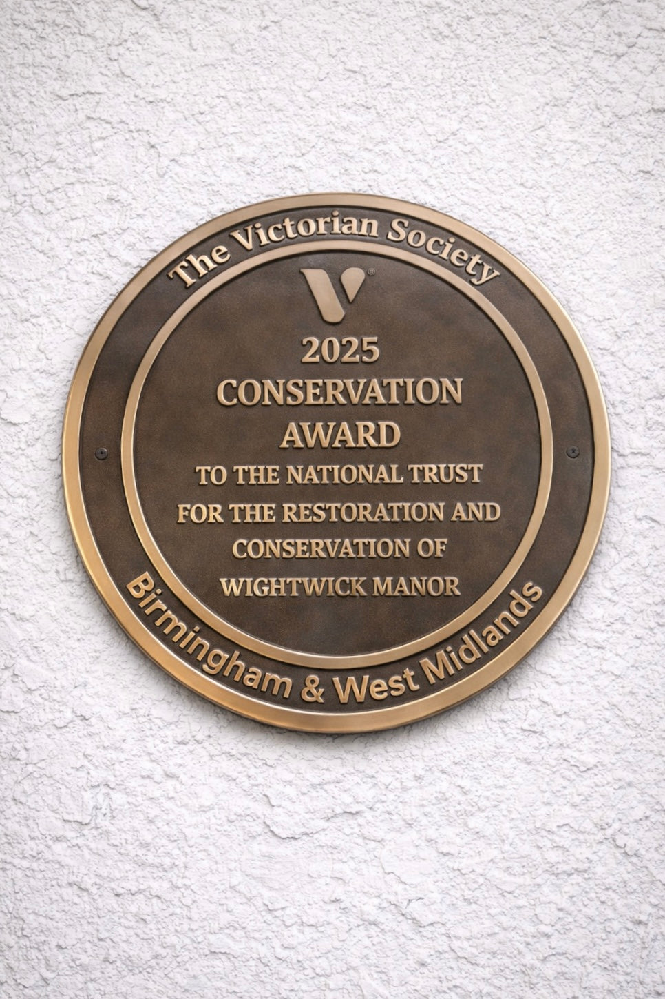Cast bronze circular heritage plaque with raised lettering mounted on exterior wall