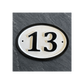 An oval house number plaque displaying '13' in black on a cream background with a black border, mounted on a dark gray slate-textured wall.