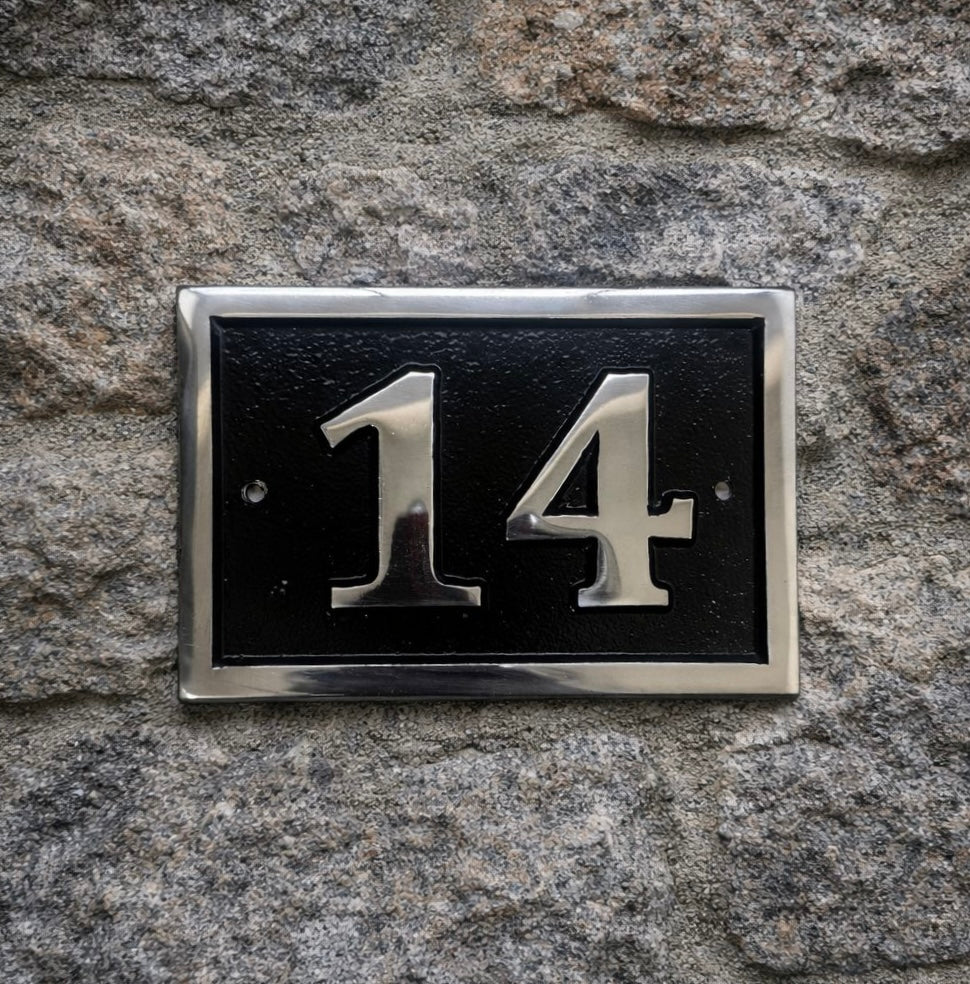 House number '14' on a black plaque with silver border mounted on a stone wall.