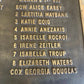 Close-up of a dark metal commemorative plaque with raised gold-colored engraved names and text.