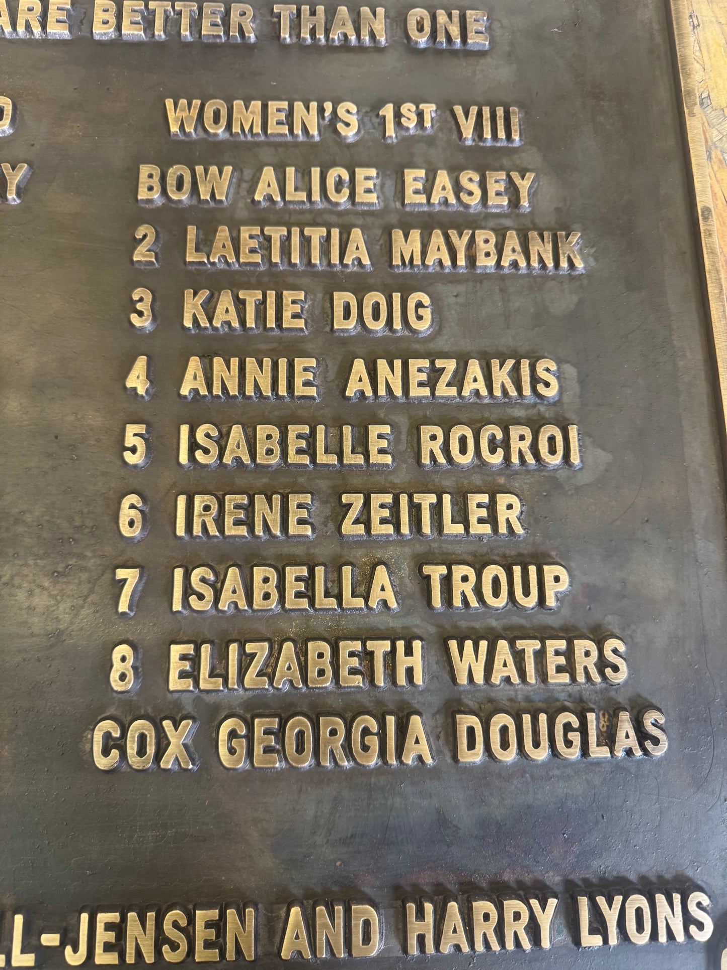 Close-up of a dark metal commemorative plaque with raised gold-colored engraved names and text.