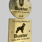 Two brass plaques commemorating a dog named Buster with his lifespan on a gray background.