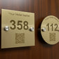 Two gold hotel room number signs with QR codes on a white wall.