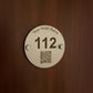 Round metal hotel room keycard with QR code and placeholder text 'Your Hotel Name' on a white background