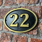 Cast aluminium oval hotel room number sign with raised numbers and black background mounted on wall