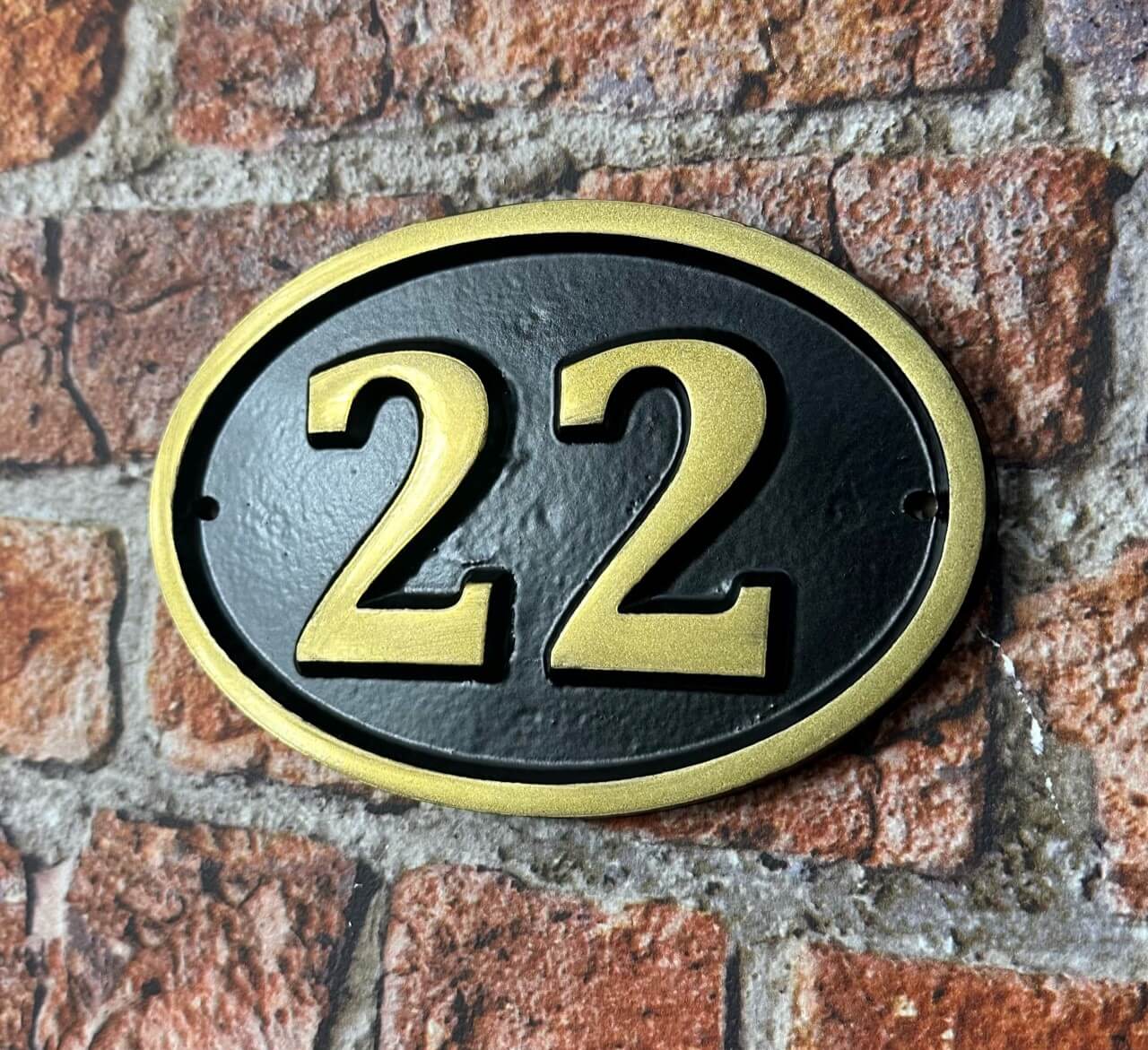 Cast aluminium oval hotel room number sign with raised numbers and black background mounted on wall